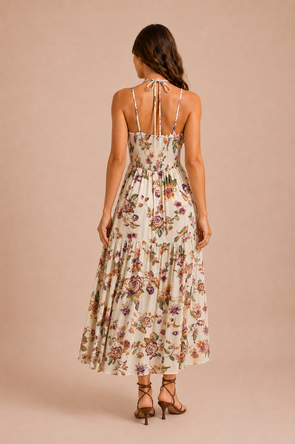 A woman in front of a beige backdrop wearing a white flowy dress featuring a multicolored floral print throughout it. 