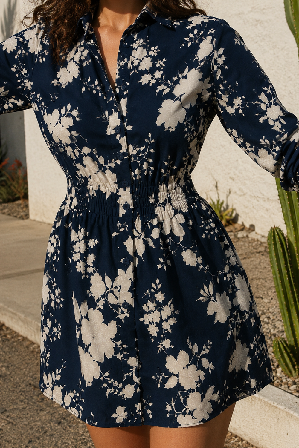A woman wearing a navy blue and white floral print mini dress with a smocked waist, standing outdoors next to a cactus.