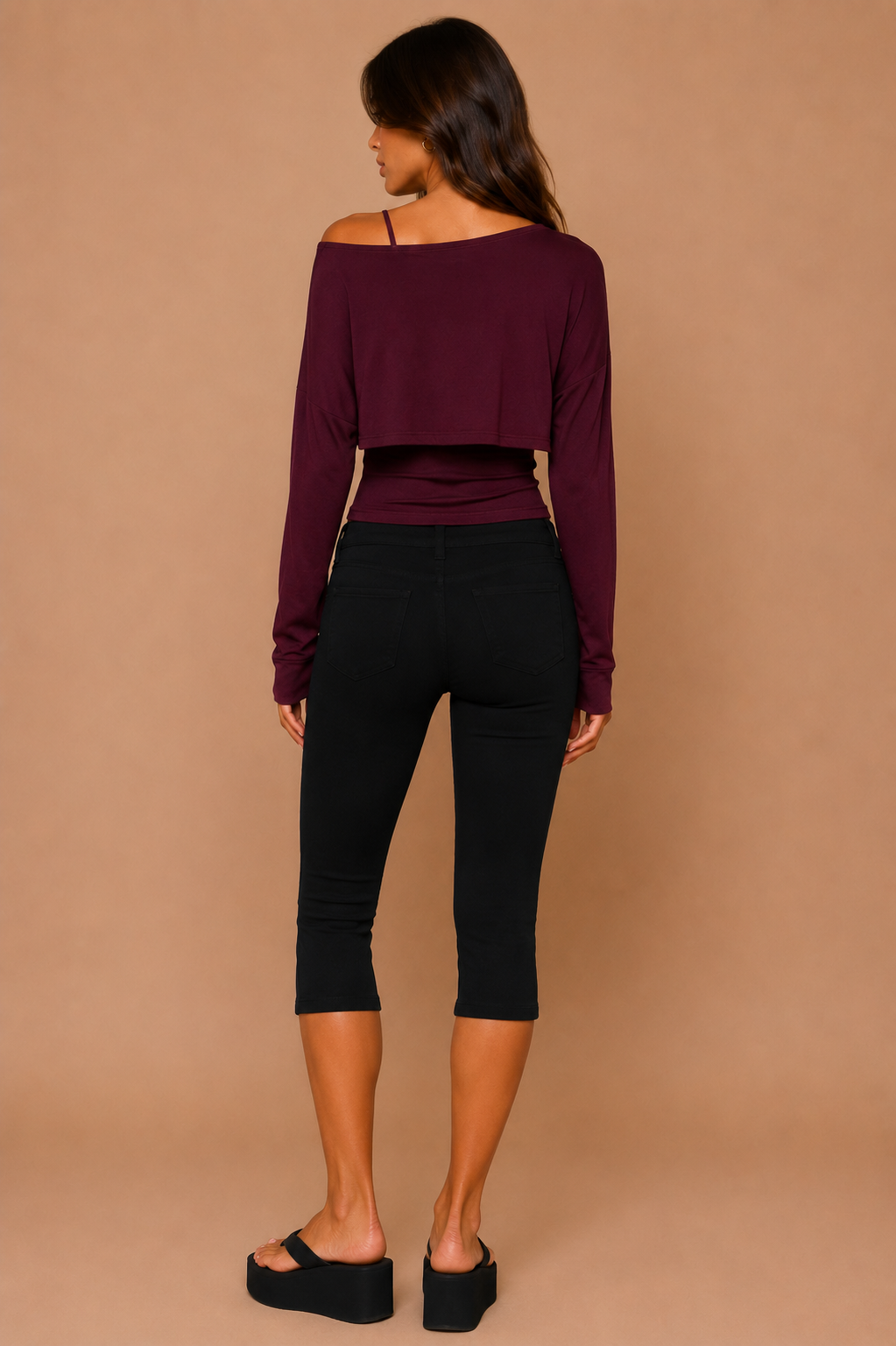 Woman wearing a burgundy long-sleeve top and black capri pants against a beige background