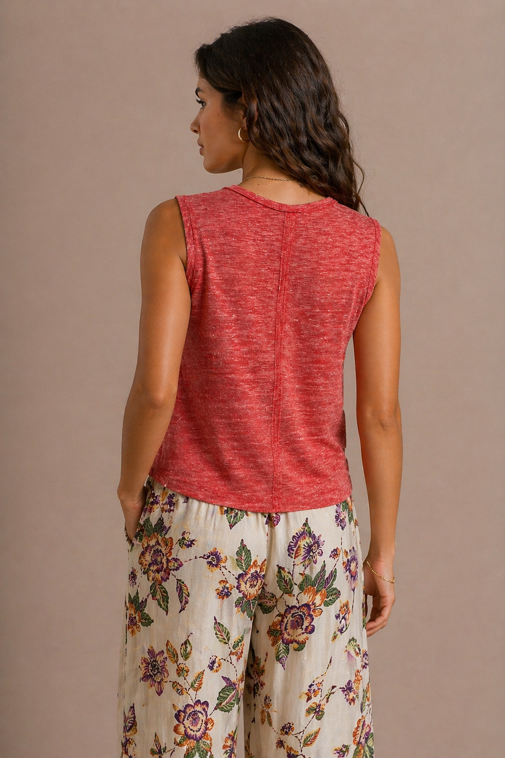 Woman wearing a red sleeveless top and floral pants against a beige background