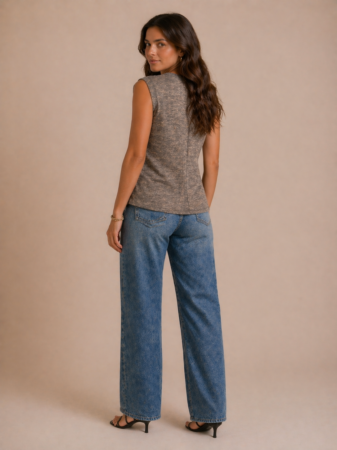 Woman wearing a sleeveless gray top and blue jeans against a beige background