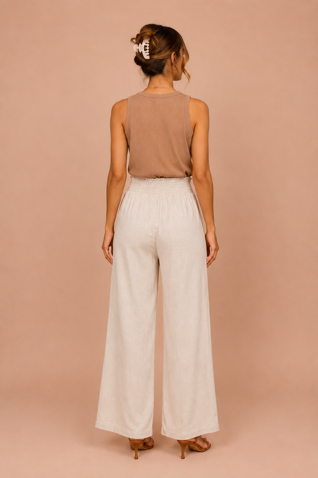 Woman wearing a brown sleeveless top and white wide-leg pants against a beige background