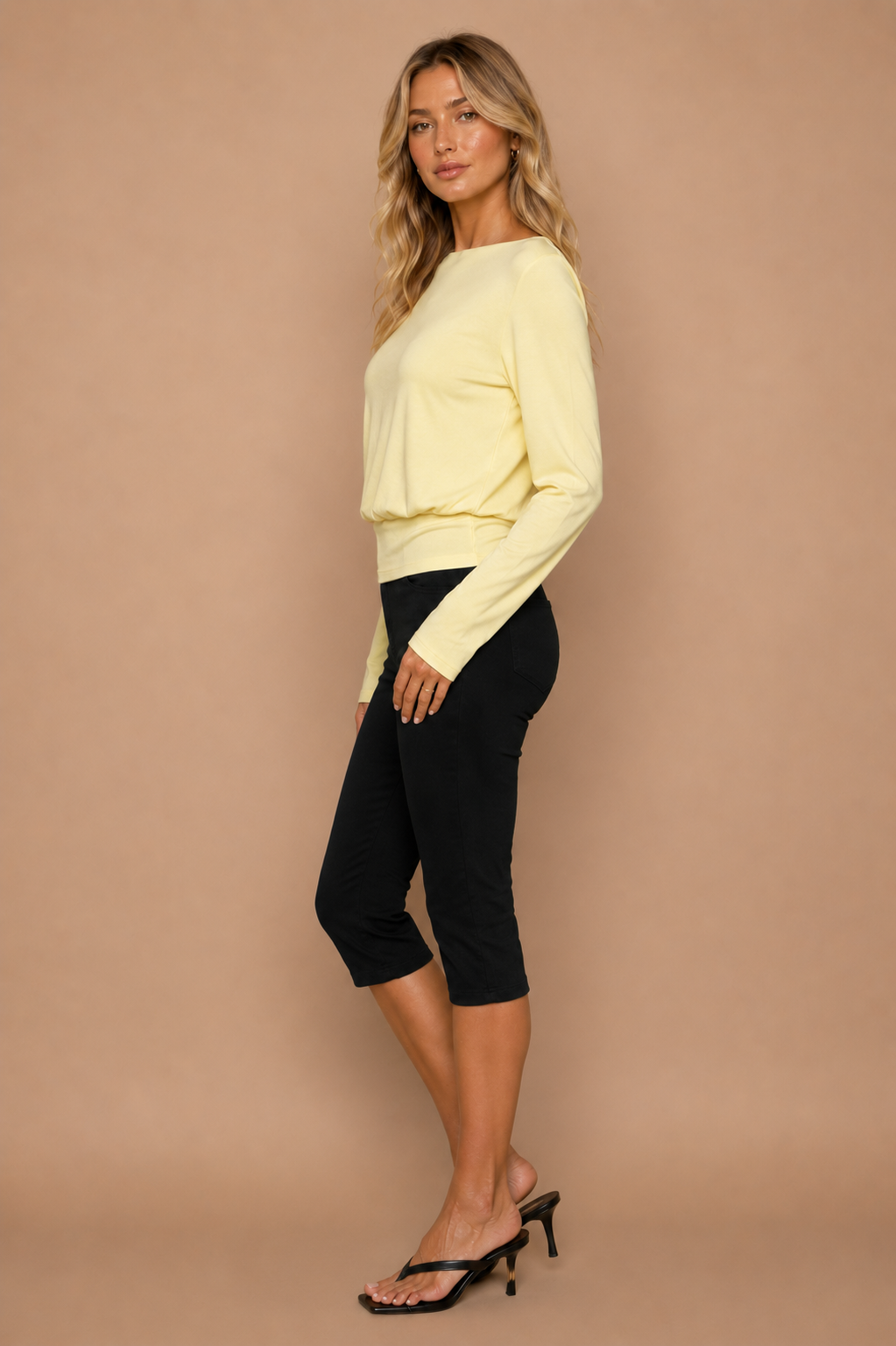 Blonde woman wearing yellow top and black capri pants in front of beige backdrop.