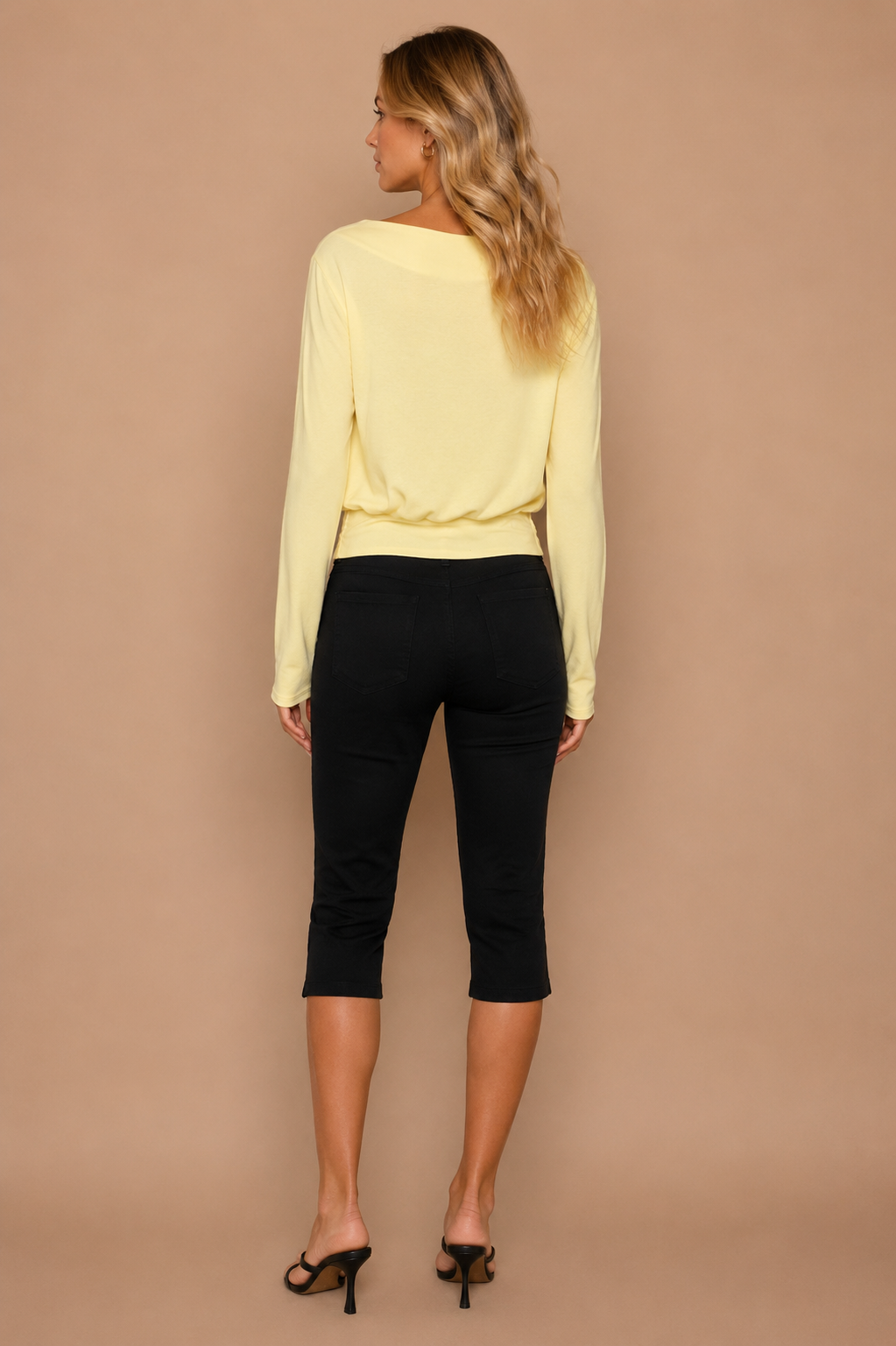 Blonde woman wearing yellow top and black capri pants in front of beige backdrop.