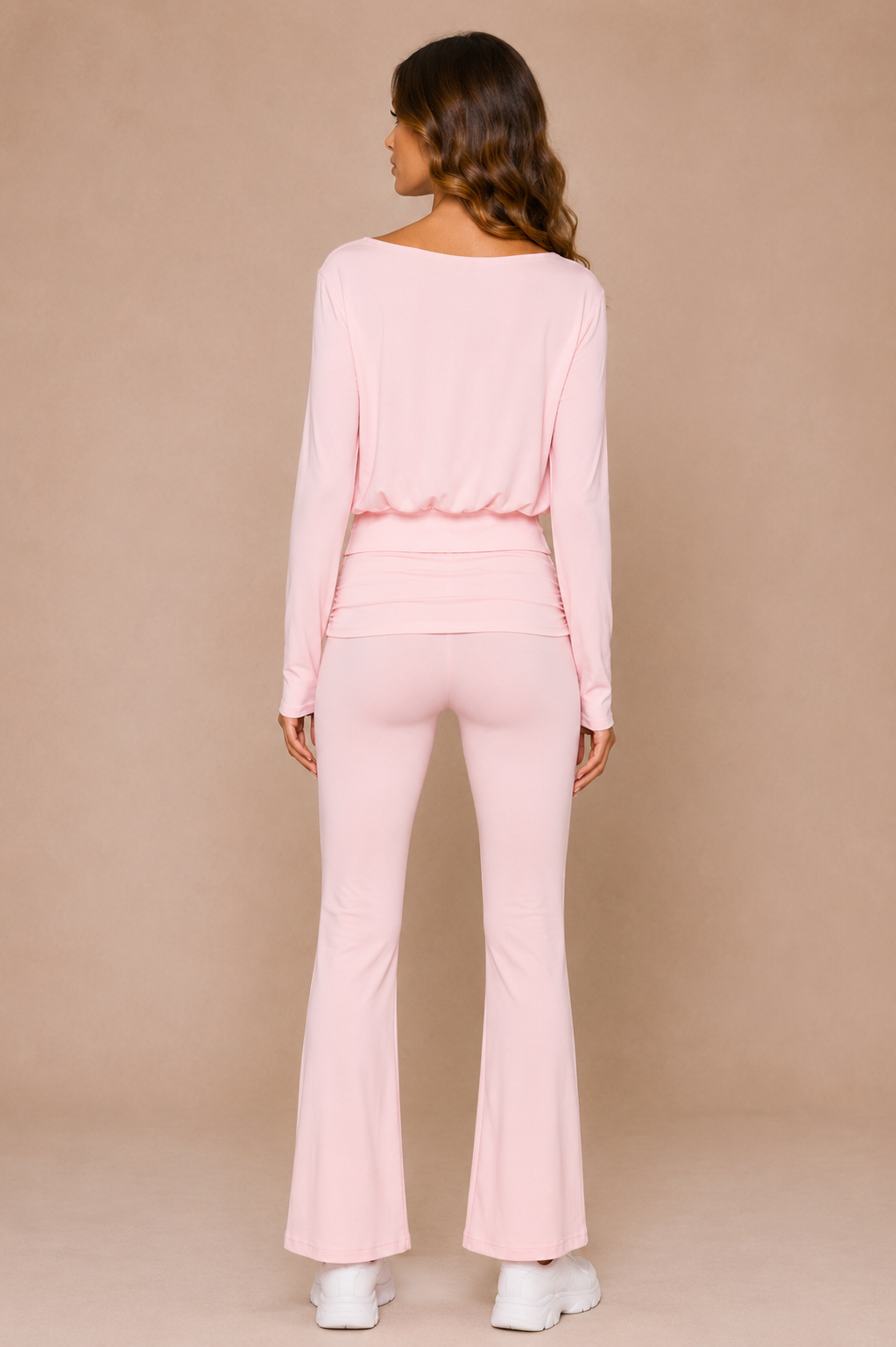 Brunette woman wearing pink top and matching pink yoga pants in front of beige backdrop.