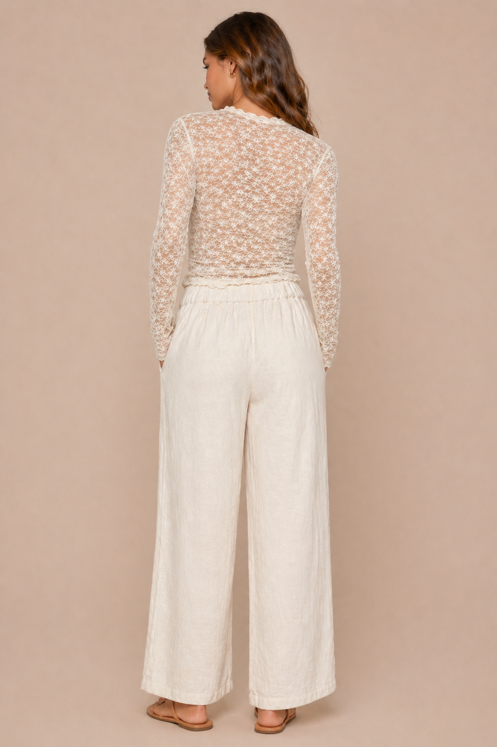 Woman wearing a sheer long-sleeve top and wide-leg pants against a beige background