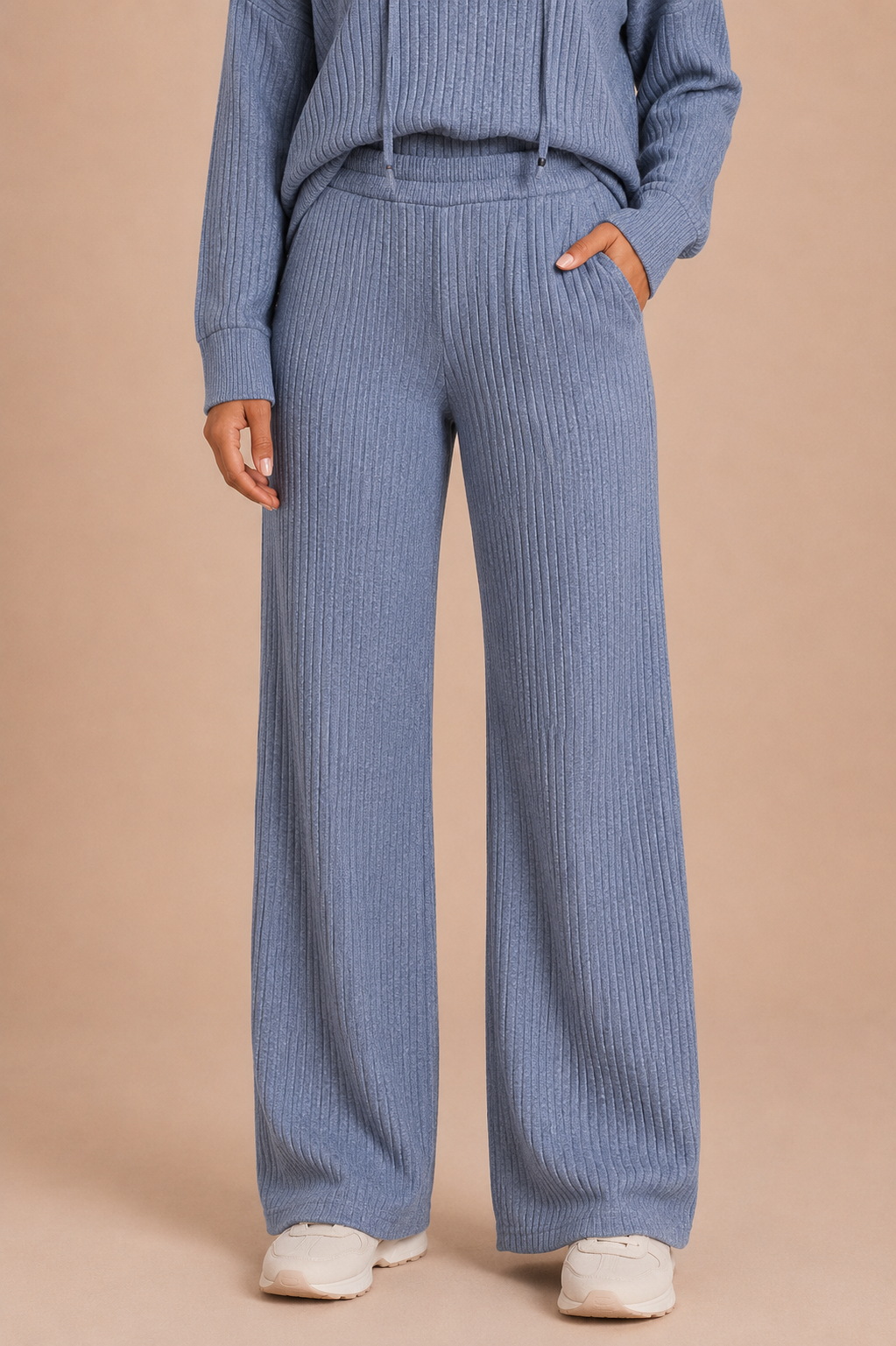 Person wearing blue ribbed pants and a matching hoodie on a beige background