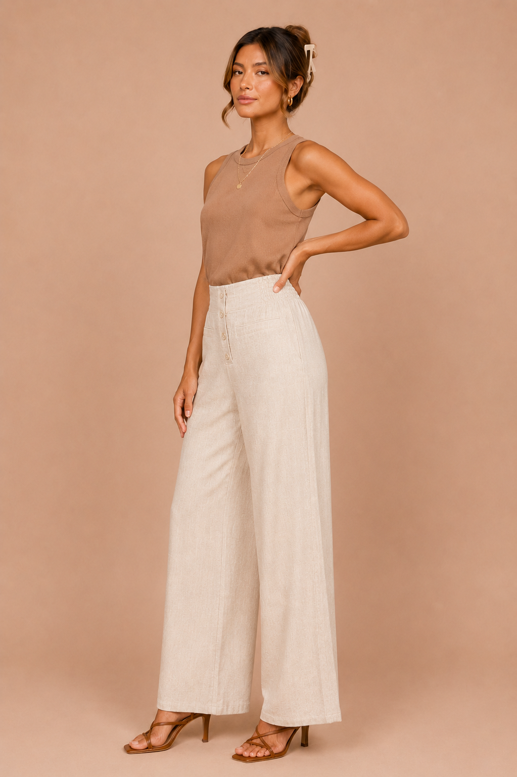 Woman wearing a brown sleeveless top and white wide-leg pants against a beige background
