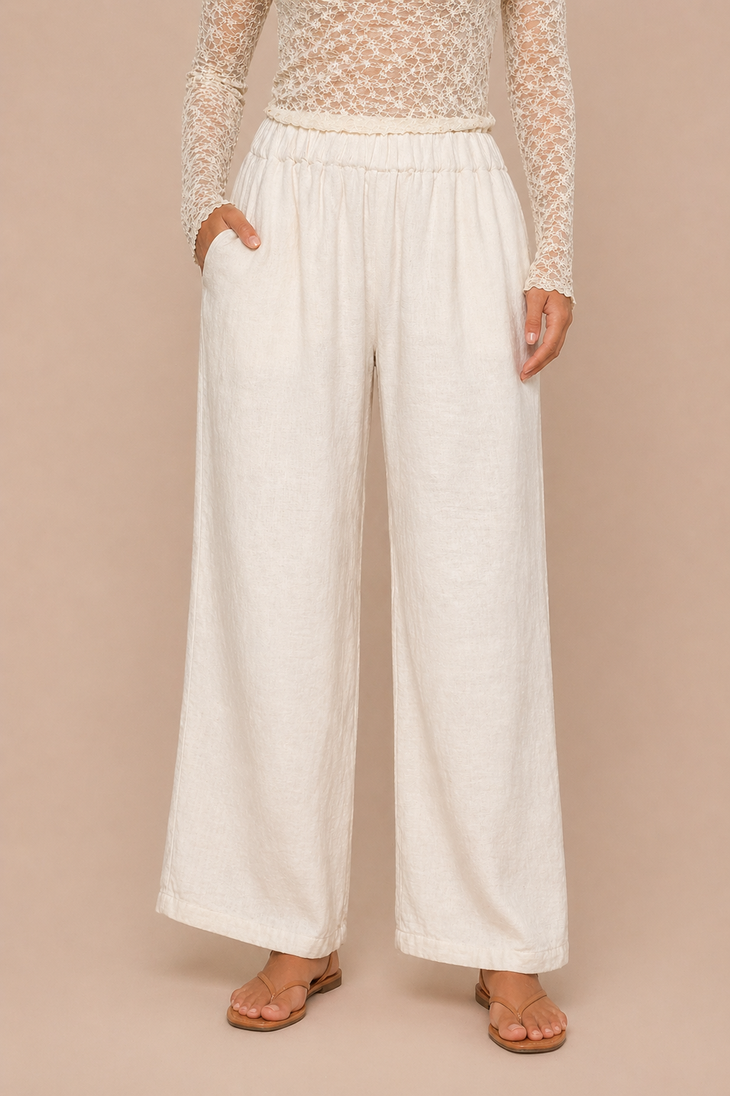 Person wearing a lace top and white wide-leg pants on a beige background