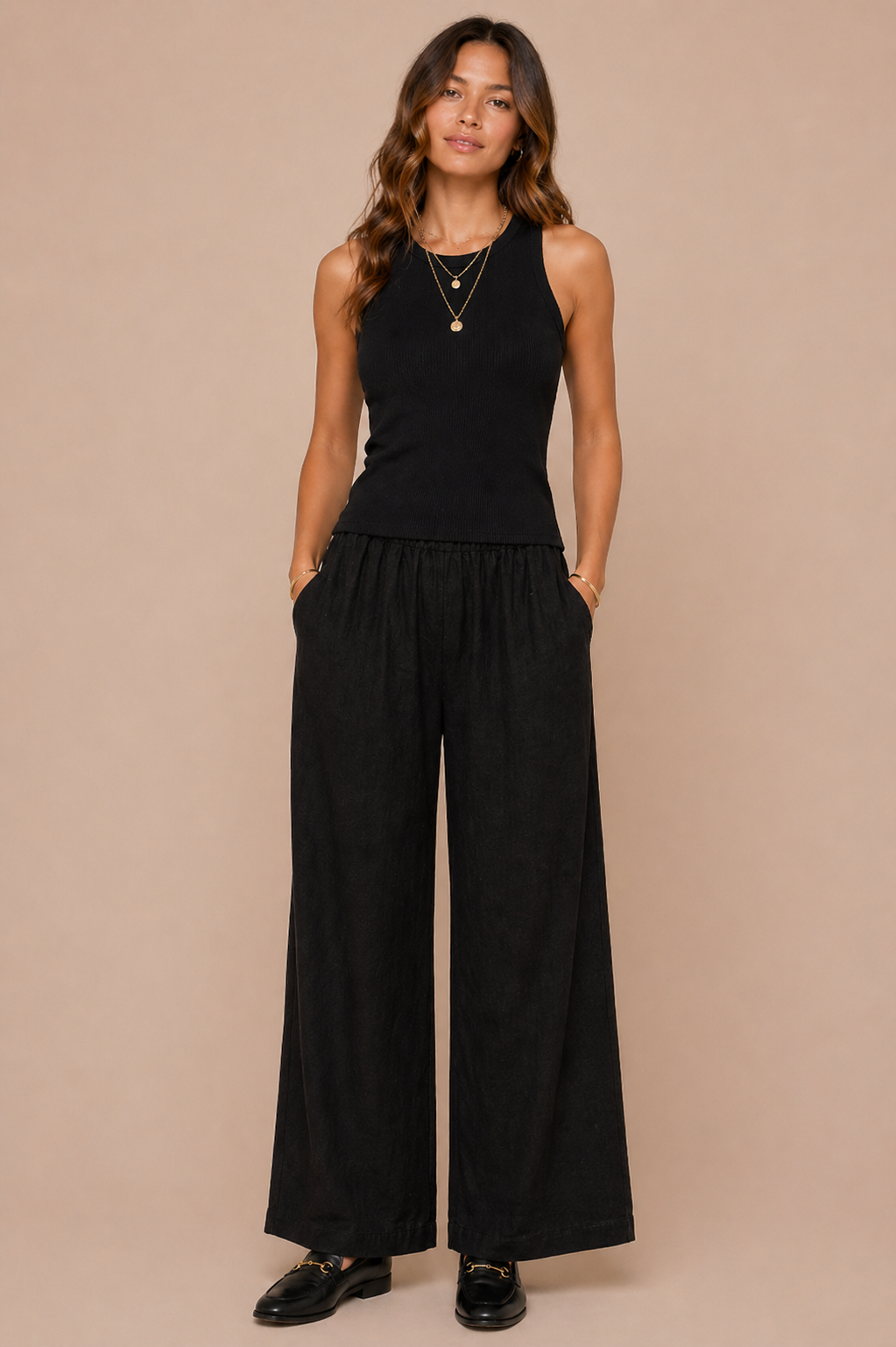 Woman wearing a black sleeveless top and wide-leg pants against a beige background