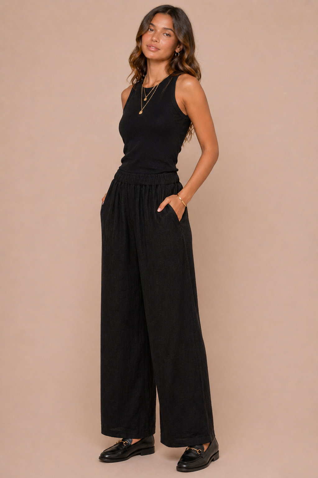 Woman wearing a black sleeveless top and wide-leg pants against a beige background