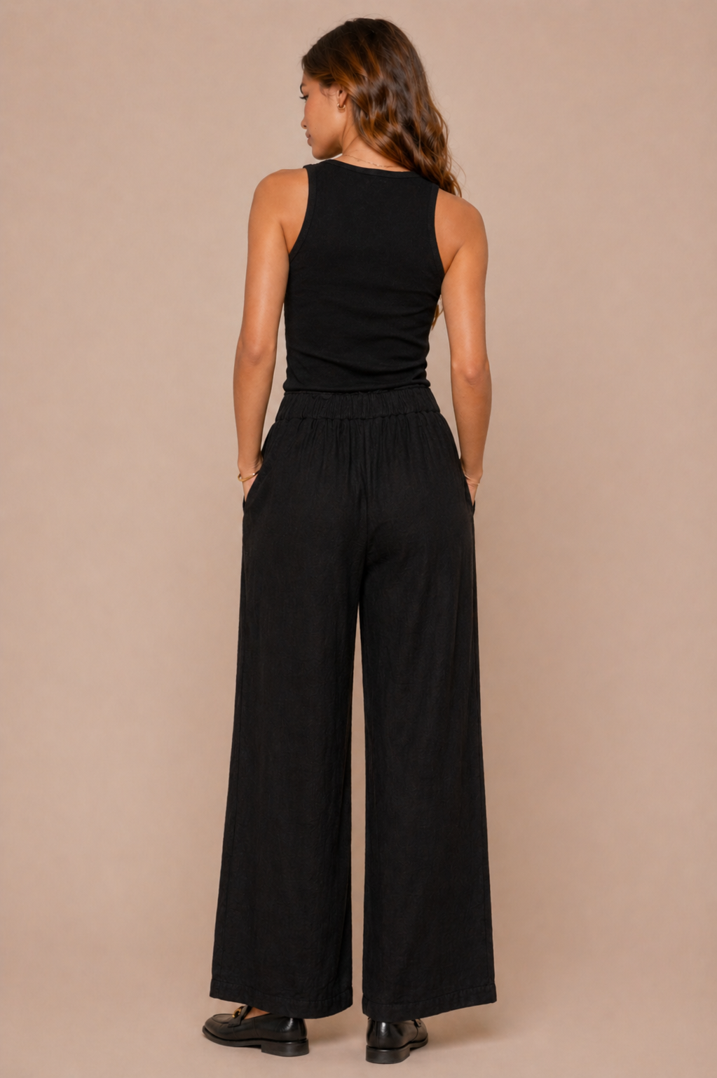 Woman wearing a black sleeveless top and wide-leg pants against a beige background