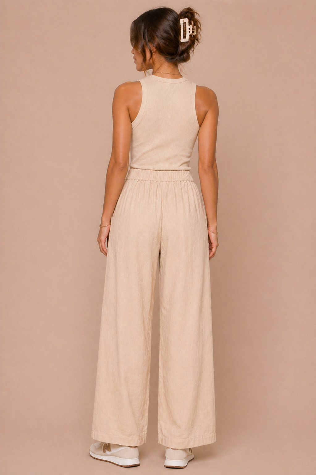 Woman wearing a beige sleeveless top and wide-leg pants against a beige background