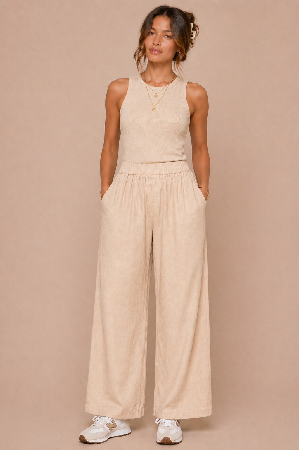 Woman wearing a beige sleeveless top and wide-leg pants against a beige background