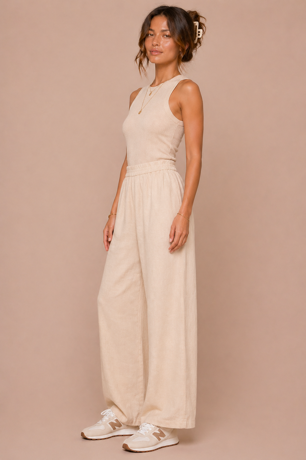 Woman wearing a beige sleeveless top and wide-leg pants against a beige background