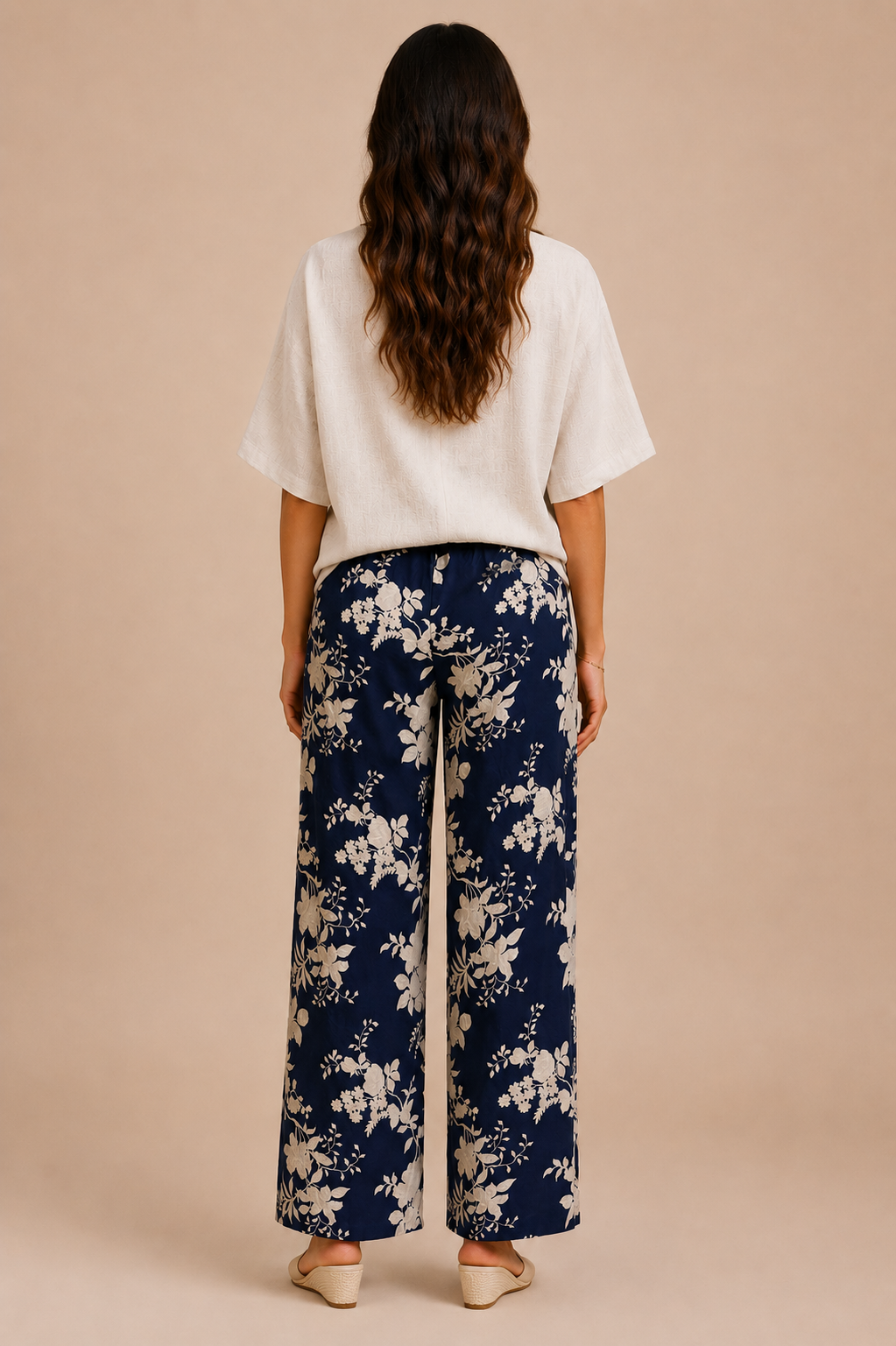 Woman wearing a white top and navy floral pants on a beige background