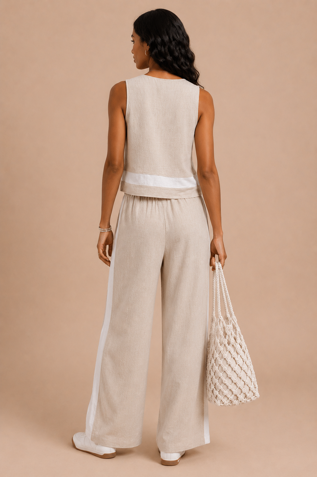 Woman wearing a beige sleeveless top and wide-leg pants, holding a white mesh bag on a beige background.