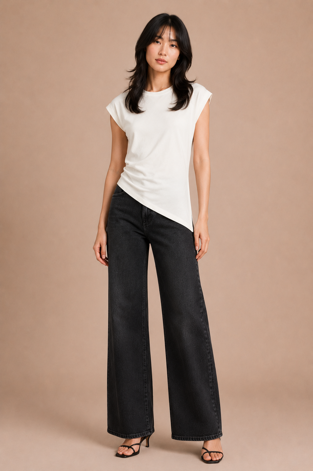 Woman wearing white asymmetrical top and black jeans against beige backdrop.