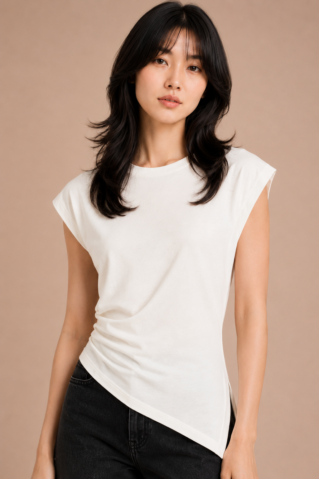 Woman wearing white asymmetrical top and black jeans against beige backdrop.