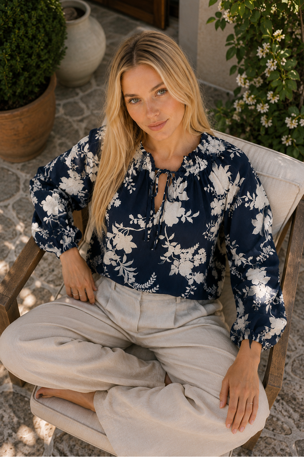 Woman sitting outdoors wearing a navy floral blouse and light pants.