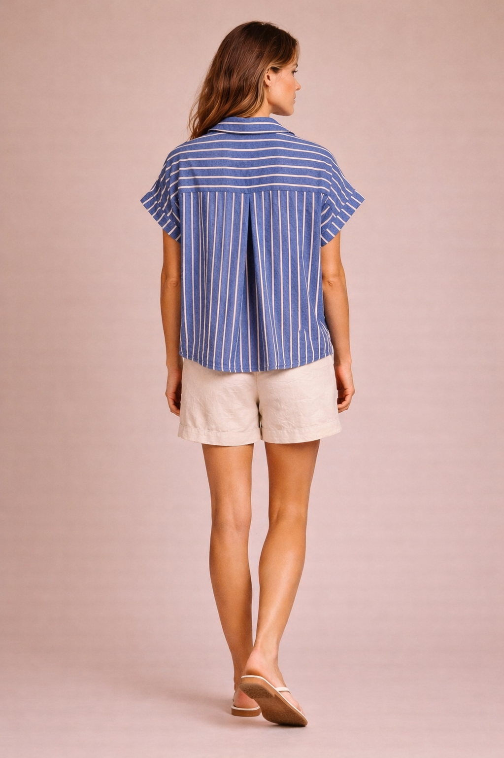 Woman wearing a blue striped shirt and white shorts on a beige background